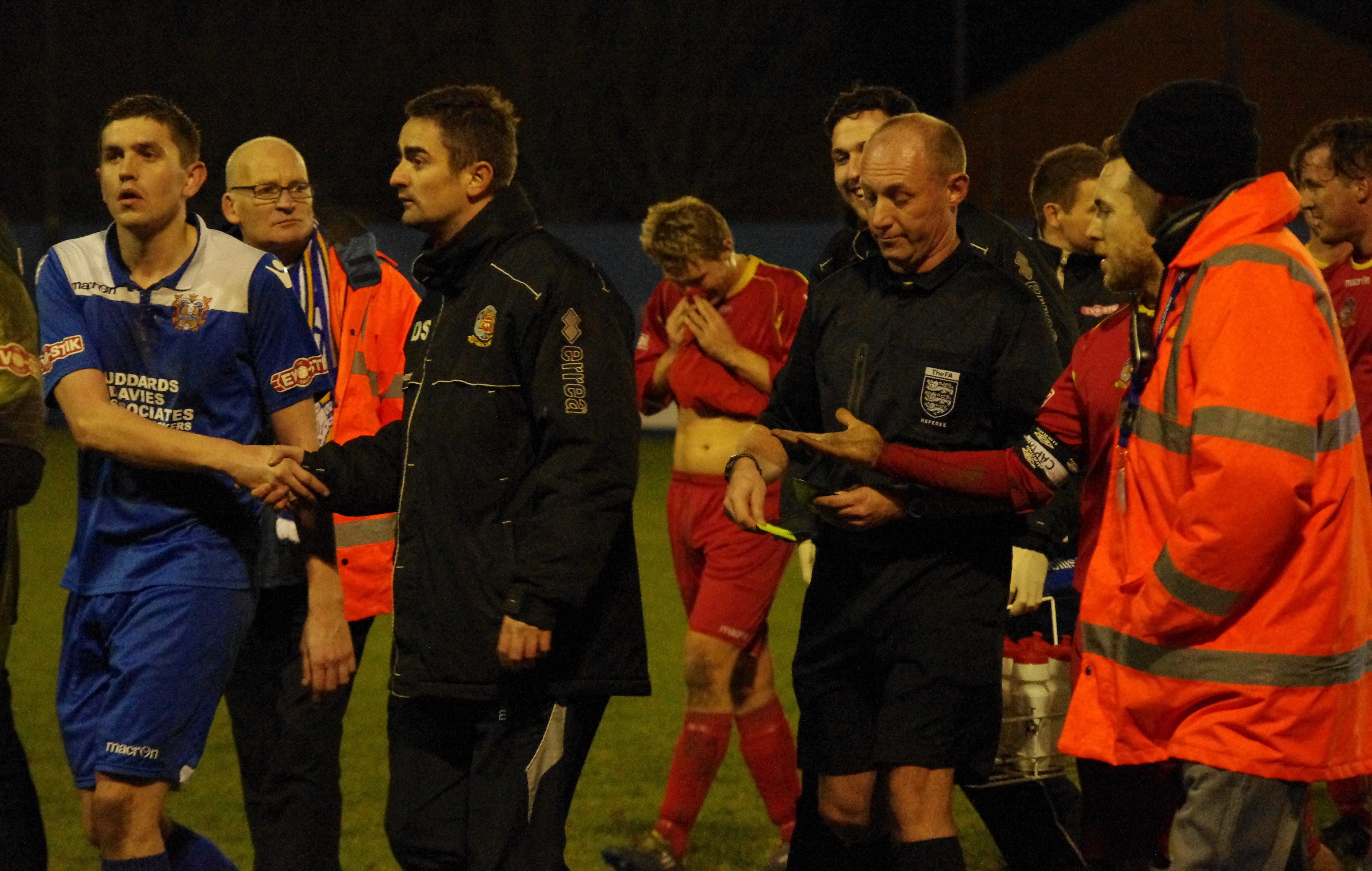 Referee David Benton is escorted off after declining Craig Elliott's handshake