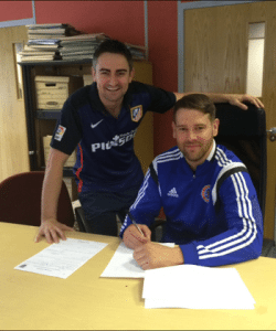 Shaw Lane assistant manager Daz Smith watches star striker Gav Allott sign his form 